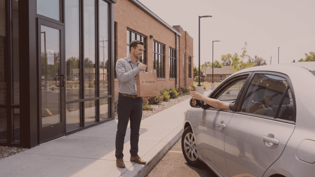 Cannabis Adviser handing product bag to customer in car at Fluresh curbside pickup lane next to brick dispensary building